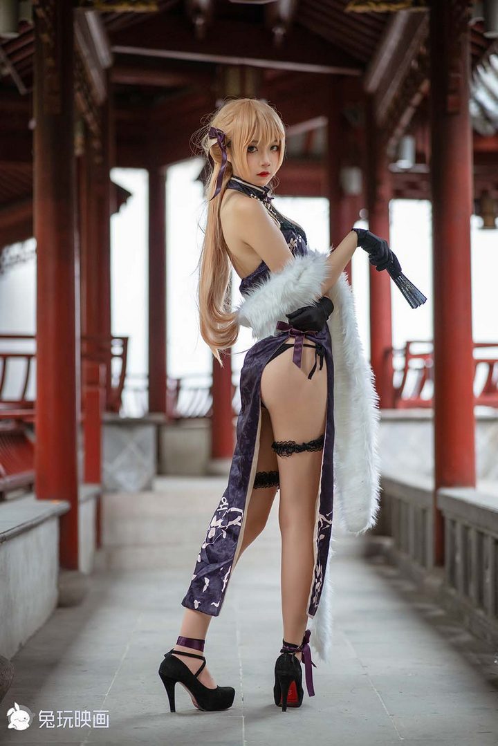 一位金色长发的Coser扮演国风妖姬，身穿一件紫色的高开衩改良旗袍，搭配白色毛绒披肩，站在中式回廊里。