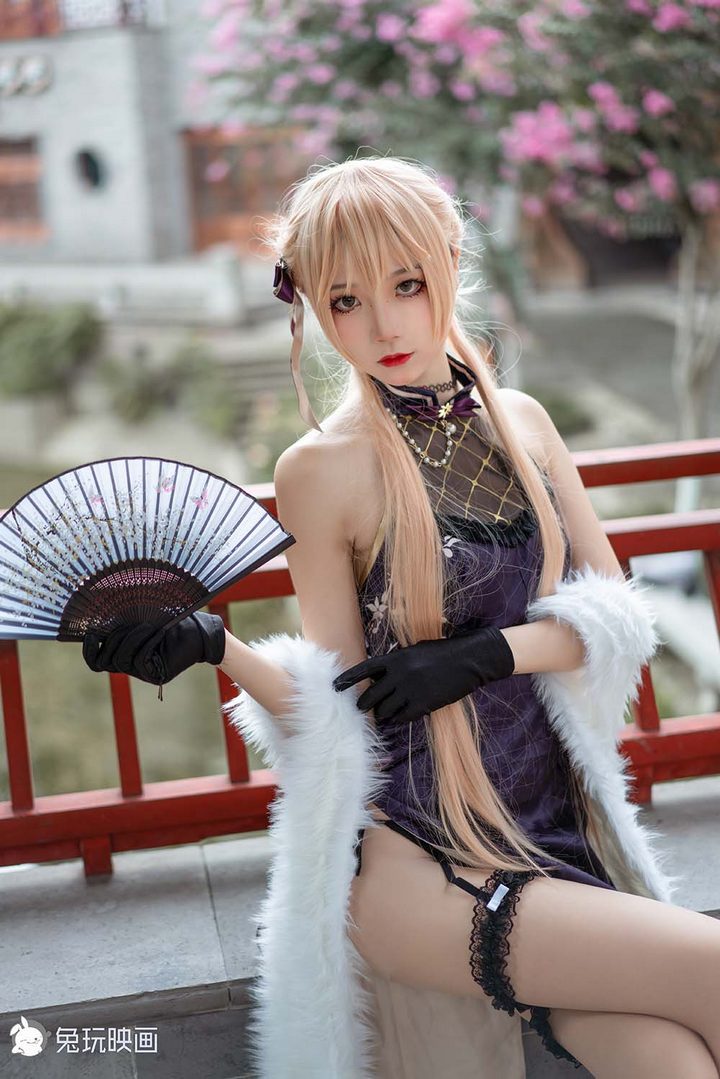 一位金色长发的Coser扮演国风妖姬，身穿一件紫色的高开衩改良旗袍，搭配白色毛绒披肩，站在中式回廊里。