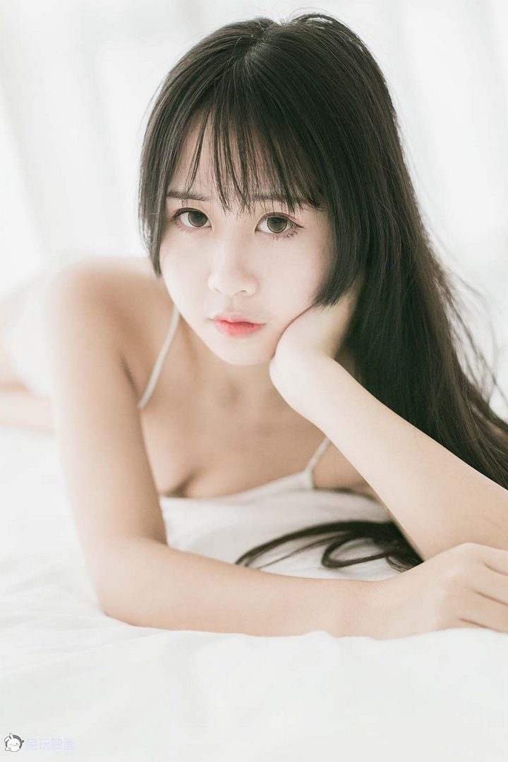 一位留着齐刘海、长发及腰的清纯少女，身穿白色吊带背心和短裤，坐在洁白的床上。