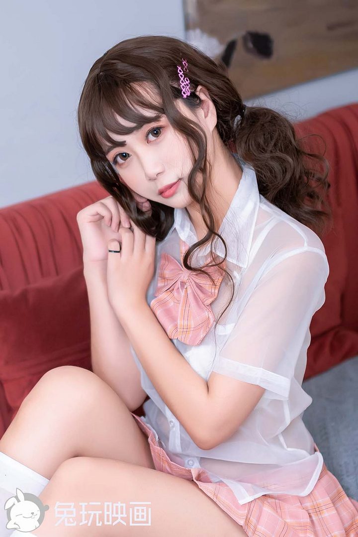 一位可爱的萌系学妹，留着刘海，身穿粉色格子裙和半透明的JK制服衬衫，坐在沙发上。