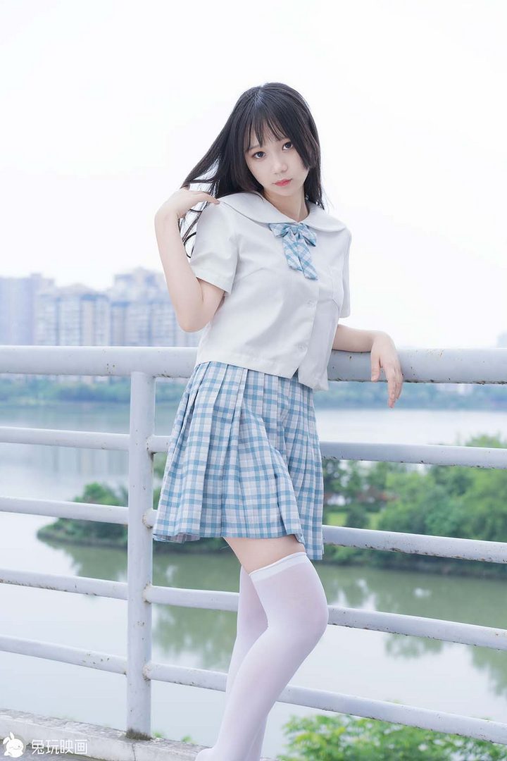 一位留着齐刘海的可爱学妹，身穿蓝白格子裙的JK制服和白色长袜，在户外的栏杆旁。